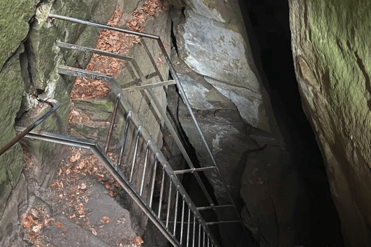A metal staircase descends between moss-covered rock walls into the dark Wolf's Gorge at Echternach